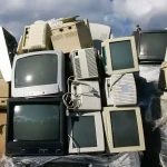 Stack of obsolete CRT computer monitors and old office desktop casings ready for asset recovery segregation